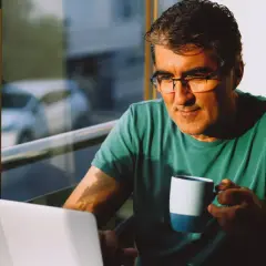 Mężczyzna w okularach z kubkiem kawy przed laptopem, zastanawia się, czy jestem inteligentny.